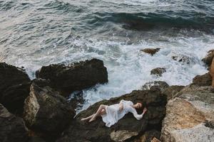 attractive woman with long hair in a secluded spot on a wild rocky coast in a white dress vacation concept photo