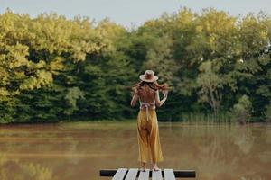 A woman stands on a lake bridge and looks out over a beautiful view in yellow pants and a hippie fall look photo