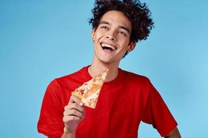 energético chico con un rebanada de Pizza teniendo divertido en un azul antecedentes y un rojo camiseta foto