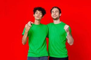 Two cheerful friends in green t-shirts communicating emotions red background photo