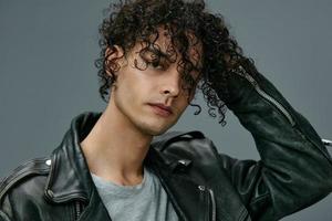 Headshot portrait of handsome stylish tanned curly man leather jacket posing isolated on over gray studio background. Cool fashion offer. Huge Seasonal Sale New Collection concept. Copy space for ad photo