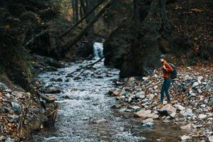 mujer turista en calentar ropa con un mochila en el río banco y alto arboles paisaje foto