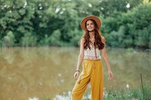 un joven mujer en un hippie Mira viajes en naturaleza por el lago vistiendo un sombrero y amarillo pantalones en el otoño foto