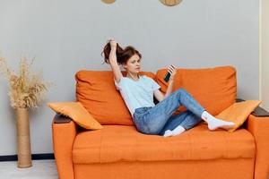 alegre mujer chateando en el naranja sofá con un teléfono inteligente apartamentos foto