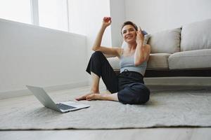 Freelance woman with laptop and phone works from home sitting on the floor in her home clothes with a short haircut, free copy space photo