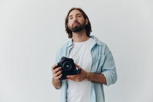 Man hipster photographer in a studio against a white background holding a professional camera and setting it up before shooting. Lifestyle work as a freelance photographer photo