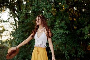 un mujer en Respetuoso del medio ambiente ropa en un hippie Mira bailes en naturaleza en el parque y sonrisas a el mundo. el concepto de armonía con el cuerpo y el rodeando naturaleza foto