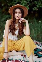 hermosa joven niña de cerca mira dentro el cámara en un sombrero vistiendo un eco hippie al aire libre, hermosa sonrisa con dientes en el puesta de sol ligero foto