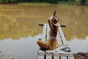 A woman yogi sits with her back to the riverbank on a bridge and meditates on relaxing her body in nature photo