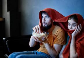 scared woman with a red plaid on her head and a man with a plate of popcorn in a dark room photo