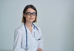 Professional woman doctor in a medical gown and glasses with a stethoscope around her neck photo