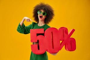 Beautiful fashionable girl green dress afro hairstyle dark glasses fifty percent in hands yellow background unaltered photo