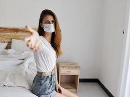 disgruntled woman in medical mask sits alone on bed in quarantine room vacation pandemic coronavirus photo