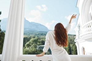 beautiful woman long hair in a white bathrobe staying on the balcony in a hotel back view photo