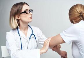 médico examina el paciente doblar su brazo en un ligero antecedentes y un estetoscopio foto