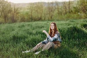 A young beautiful woman sits on the green grass in the park and looks out into the setting sun photo