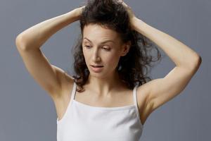 Irritated unhappy curly beautiful woman in basic white t-shirt trying to calm down hold her hair both hands posing isolated on over gray blue background. People Lifestyle Emotions concept. Copy space photo