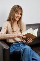 Cute happy blonde student lady with copybook read entries in her diary sitting in sofa at modern living room interior. Female client have shrink appointment in psychological help office. Copy space photo