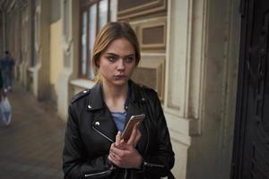 Woman on the street with a phone in her hands leather jacket walk near the building photo