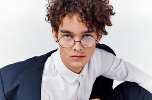 portrait of a curly-haired guy in a shirt in a jacket and glasses on a light background close-up photo