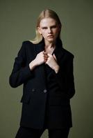 The model holds the jacket by the collar while posing on a green background in the studio. Concept photo for clothing brands. Cool offer for fashionable suits