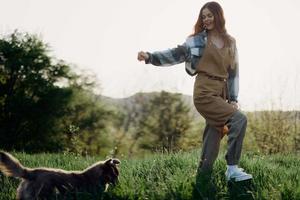 un mujer obras de teatro un juego con su pequeño perro en el verde césped en un campo en el soleado noche ligero de naturaleza. el concepto de cuidando para animales y armonía con naturaleza foto