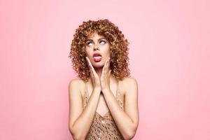 Model curly hair shows tongue look aside grimace pink background photo