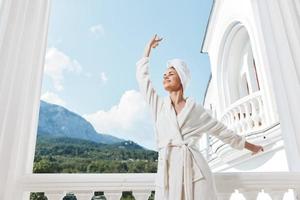 Portrait of gorgeous woman with a towel on my head in a white bathrobe staying on the balcony in a hotel Lifestyle photo