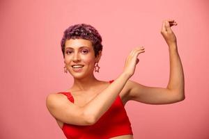 Fashion portrait of a woman with a short haircut of purple color and a smile with teeth in a red top on a pink background happiness photo