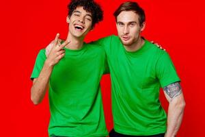 two friends in green t-shirts hugs fun red background photo