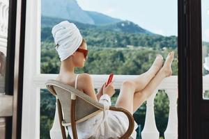 Portrait of young woman enjoying the morning on the balcony looking at the mobile phone screen Perfect sunny morning photo