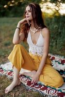 Young beautiful hippie woman sitting on the ground in nature in the autumn in eco clothing in the sunset light, a lifestyle of travel and harmony with the world photo