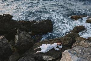 attractive woman with long hair in a secluded spot on a wild rocky coast in a white dress unaltered photo