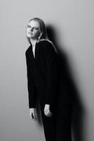 A beautiful girl in a classic suit looks into the camera leans forward posing in the studio. Black and white photo. Stylistic photography photo