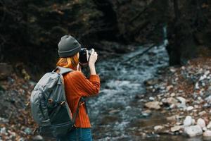woman with a camera on nature in the mountains near the river and tall trees forest landscape photo