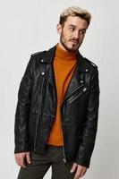 fashionable blond man in a leather black jacket and an orange sweater tilted his head to the side photo