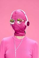 Woman art beats conceptual portrait on bright pink wax wearing shiny neon glasses, pink mask and headphones photo