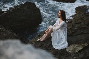 A woman in a white wedding dress is sitting barefoot on a wave cliff unaltered photo