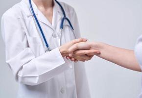 Professional doctor woman shakes hand of a female patient on a light background photo