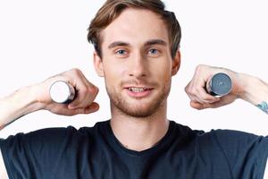 a sporty man in a black t-shirt holds dumbbells near his face on a light background and a black t-shirt photo