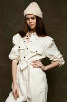 fashionable brunette in a white hat and jumpsuit posing against a dark background photo