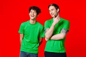 joyful friends in green t-shirts are standing next to red background photo