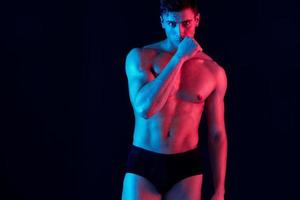 sexy male athlete gesturing with his hands on a black background and neon skin color model photo