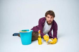 A man lies on the floor with a bucket of detergent cleaning service light background photo