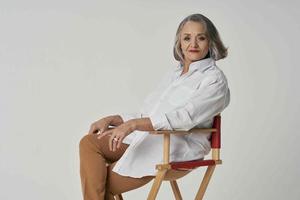 aged woman in white shirt sits on a chair red lips isolated background photo