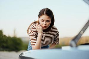 A woman with a wrench looks sadly and sadly under the open hood of her car and can't fix it from a roadside breakdown while traveling alone photo