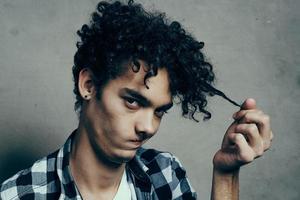 guy in a t-shirt and in a plaid shirt examines his hair on a gray background cropped view close-up photo