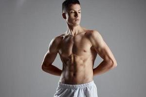 athlete with pumped up abs holding hands behind his back on gray background photo