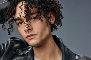 Closeup portrait of stylish tanned curly man leather jacket posing isolated on over gray studio background. Cool fashion offer. Huge Seasonal Sale New Collection concept. Copy space for ad photo