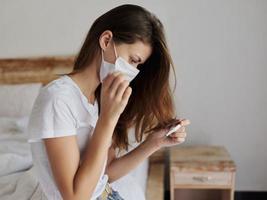 woman looking at thermometer in medical mask checking temperature photo